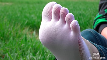 Goddess feet in cute white socks with jeans on the spring grass field