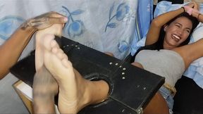 Julio tickles Ana Karina's feet in the stocks