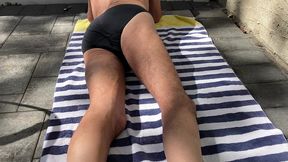 laying in the sun on striped towel and stretching away the pain in dark tight briefs