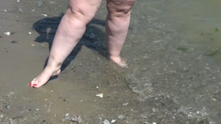 Fat bare legs with red pedicure walk along the bank of the river, fetish.
