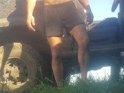 Grown man pees himself in shorts and bare feet outdoors in the grass by the dirty truck