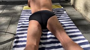 Laying in the sun on striped towel and stretching away the pain in dark tight briefs