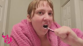 Brushing teeth with hair up and pink towel over shoulders