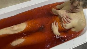 A bath in red coloured Jelly Cubes. As I scoop up the jelly cubes into a sieve, and empty them back over my body