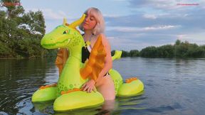 Alla rides a squeaky, glossy, medieval inflatable dragon on a lake
