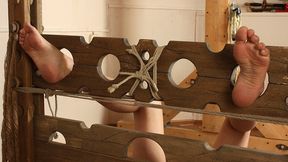 Barefoot tapegagged Irene in beige top and white shorts, lying on the floor with her feet locked in pillory, is getting her feet oiled and tickled by the man (HD MOV)