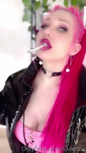 Pink haired Luvie Doll in PVC leggings and puffer jacket smoking slim line cigarette with long nails