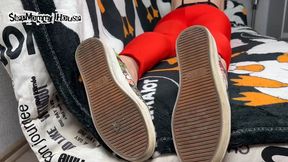 Brunette Crossed Legged in Yoga Pants lying on sofa in Stinky Shoes - Sniff the Smell of Stinky Boots, Sweaty Insoles in Sneakers, Girl Ignores Smoking, Pointing long Toes with Black Pedicure