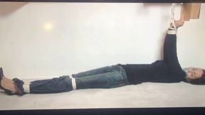 Tape-gagged brunette Gia Mancini lay stretched out and writhing on the floor with her arms tied overhead to a wooden bar!