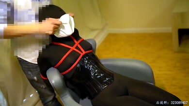 Black latex and red rope bondage session under warm light with Chinese character motif