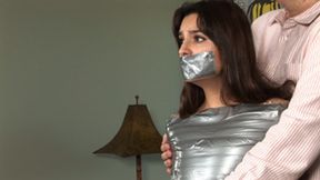 Lovely Carol Luna first stands in ankles-to-shoulders duct-tape mummification, then lies squirming on a couch!