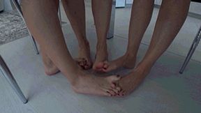 3 girls barefoot sitting at a table interlocking their toes c