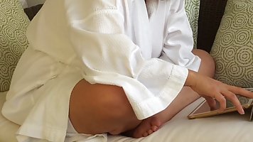 Relaxed MILF in a white bathrobe sits with no panties on her bed and reads a book
