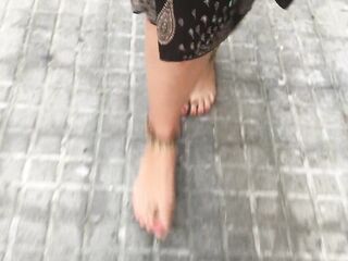 young female hippie is walking barefoot in public street