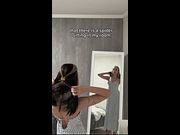 Striped dress rides up as she flexes her arm in the mirror