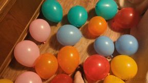 Fifi popping a floor full of balloons one by one with teasing and talking wearing single strap Birkenstocks
