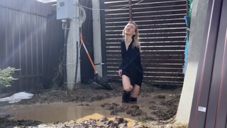 A fashionista in high-heeled boots climbed into a huge dirty pit with mud and water