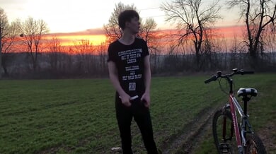 Young man with curly brown hair jerks off outdoors on a red bicycle during sunset
