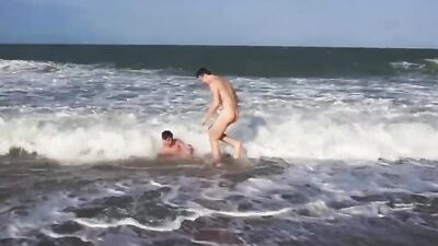 Twink gets his cock stroked by his mate on a public beach
