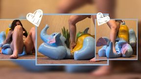 Ms. Mersiiik, in mini-shorts and barefoot, stomps very hard on a large inflatable elephant; she steps on its legs, trunk, and face, standing on it with her full weight, as well as sitting on it—sitting on its face and rubbing against it—in a display