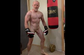 Aggressive muscular boxer working out naked with a punch bag and cums on his boxing gloves