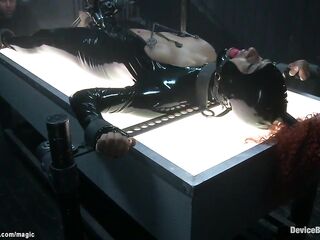Ginger black serf Daisy Ducati in latex costume shacled laid on illuminating table and snatch bibed then clamped and booty hooked on device servitude